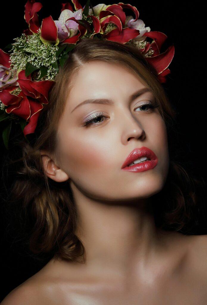 Close-up portrait of a woman with a bold floral crown on a dark background.